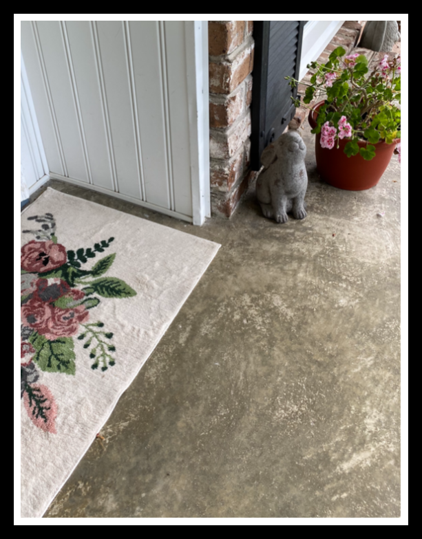 View of floral rug, gray bunny and pink geranium on inviting front porch