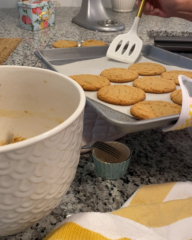 White mixing bowl with cookie dough and fresh backed cookies on baking pan