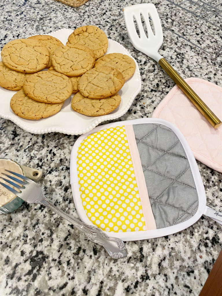 Fresh baked peanut butter cookies on plate with hot pads and spatula on black and white granite counter