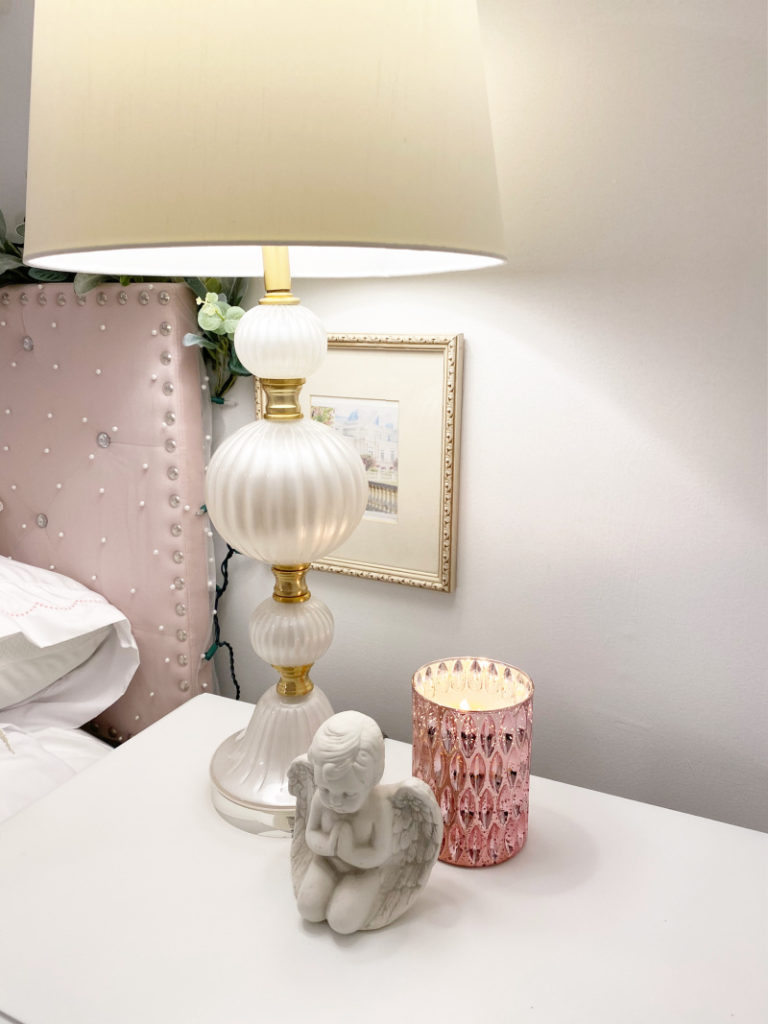 close up of cream pearl lamp, pink candle, angel and side table