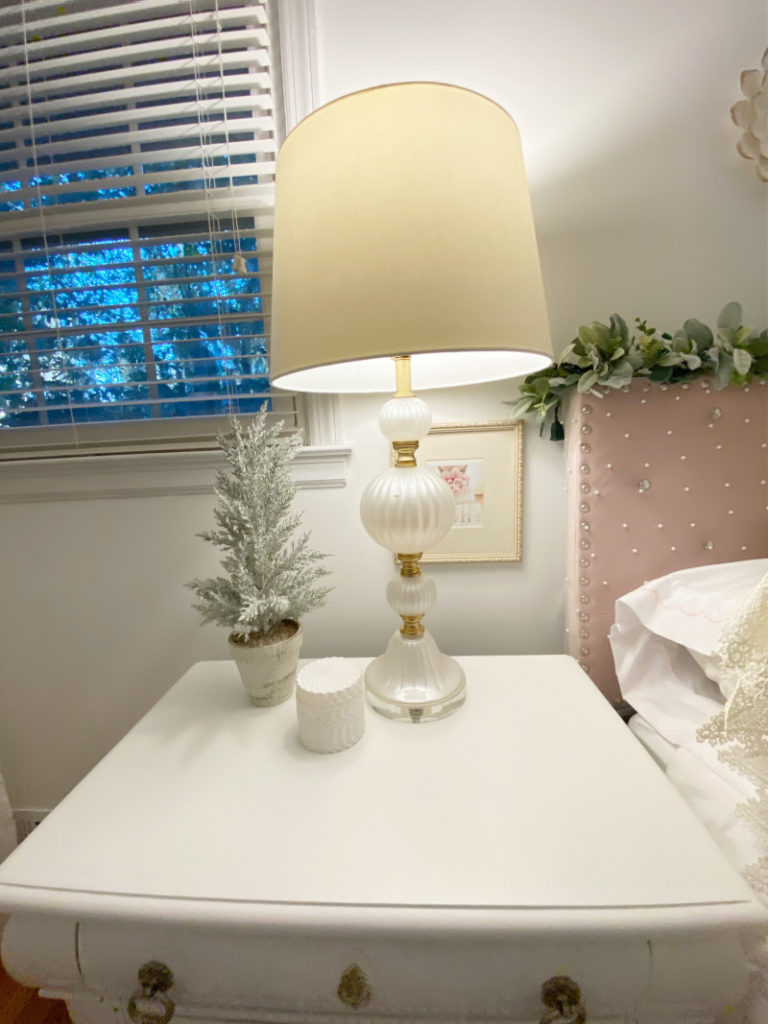 close up of cream pearl lamp, small flocked christmas tree and white candle on side table