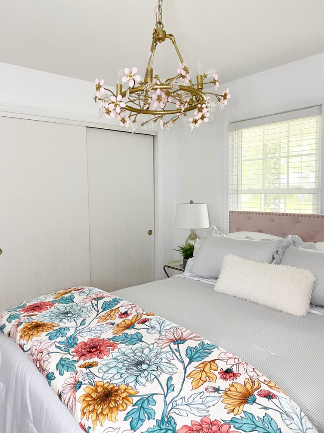 guest room made bed with floral fluffy quilt and wallpapered closet doors 
