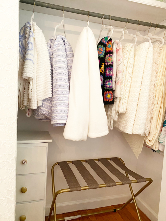 luggage rack in closet with extra blankets and throws